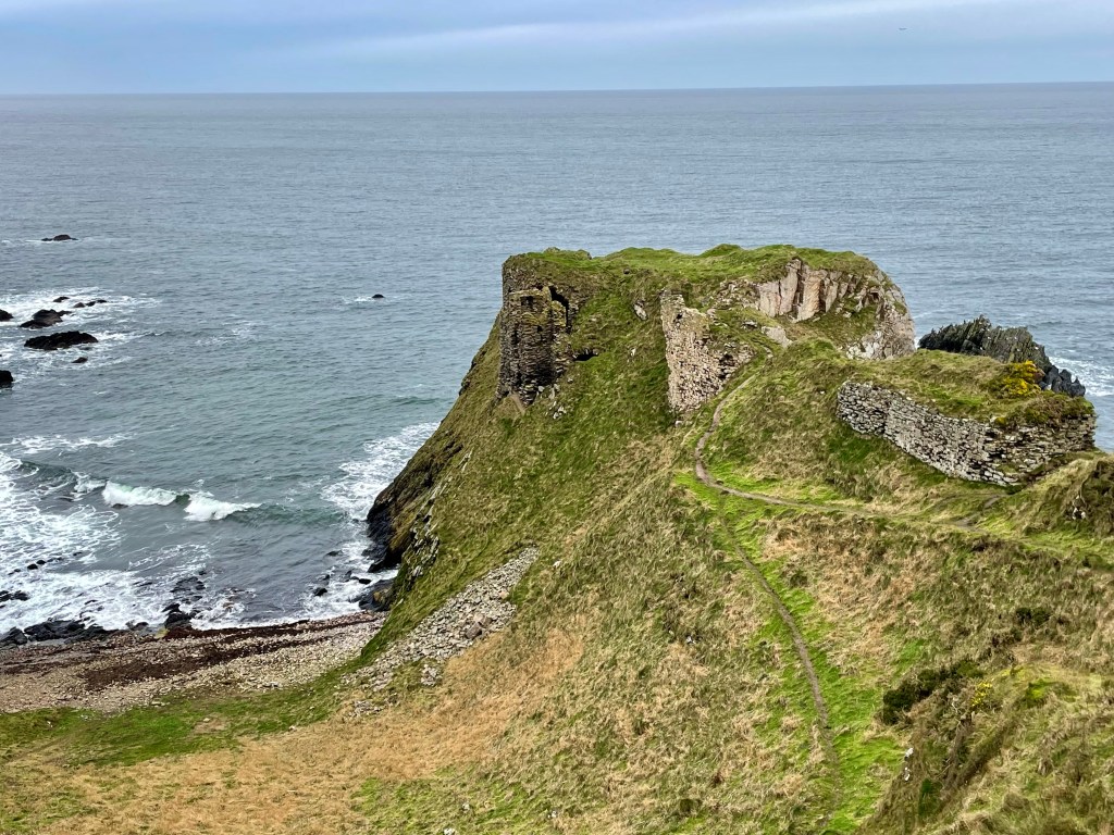 View of ruined castle in the cliffs with beach to left hand side